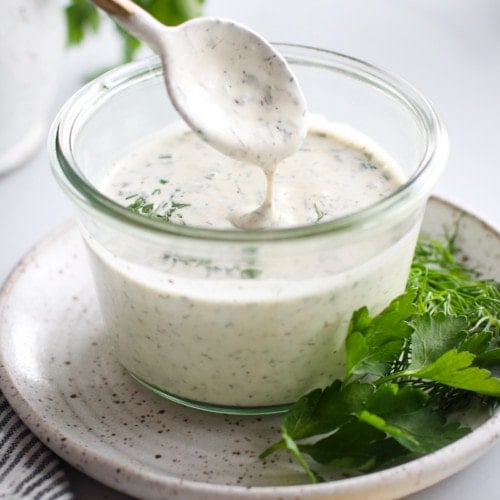 Paleo ranch dressing in a clear bowl with a spoonful on a gold spoon to show creaminess