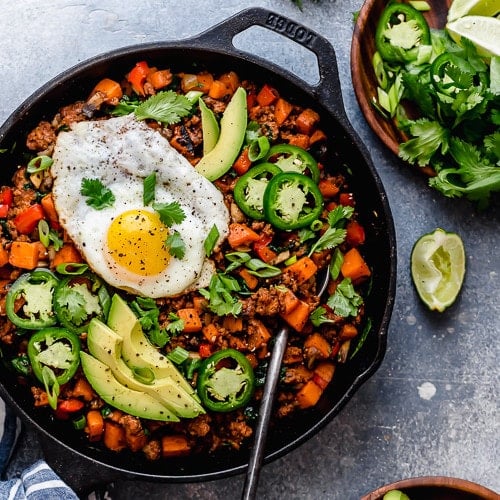 Sweet Potato Hash in a cast iron skillet and topped with a fried egg and avocado slices.