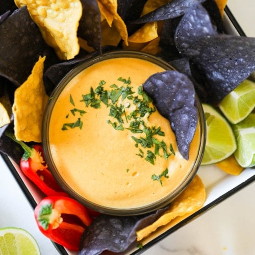 Creamy vegan nacho cheese in a small bowl surrounded with blue and yellow tortilla chips