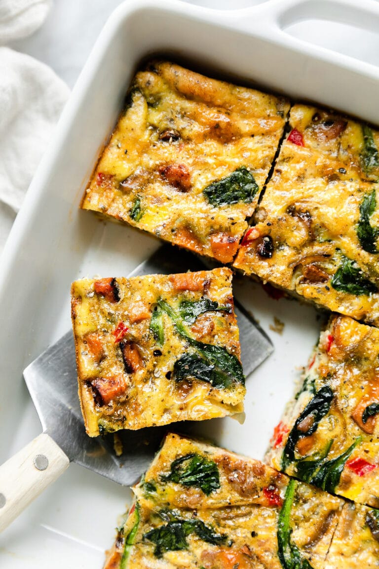 Overhead view of a sweet potato breakfast casserole cut into squares in a white baking dish. 