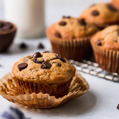 A gluten-free banana muffins topped with chocolate chips on a freshly peeled-away muffin liner.