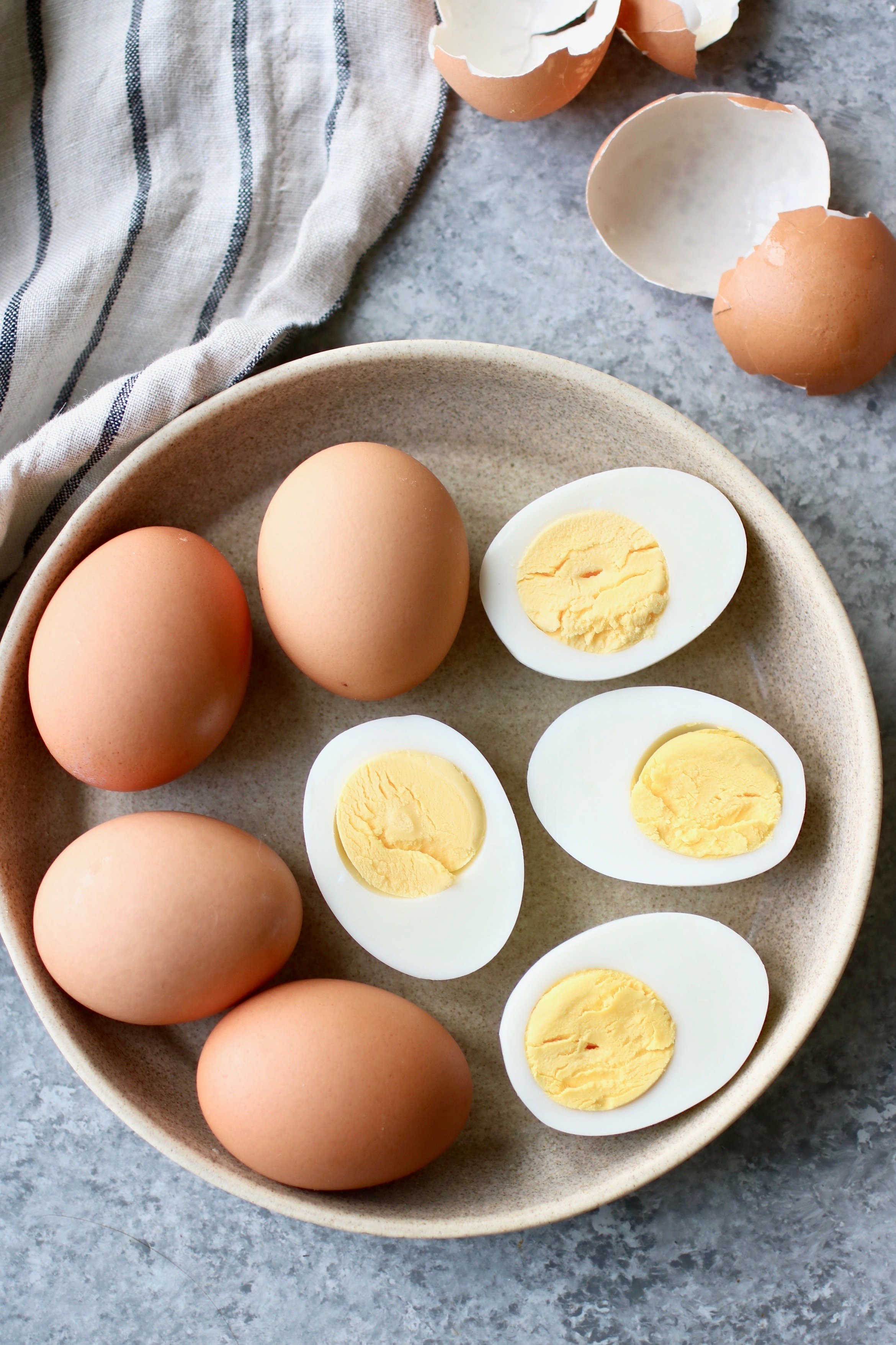 Overhead view of hard-boiled eggs and peeled and cut in half hard-oiled eggs on a plate together. 