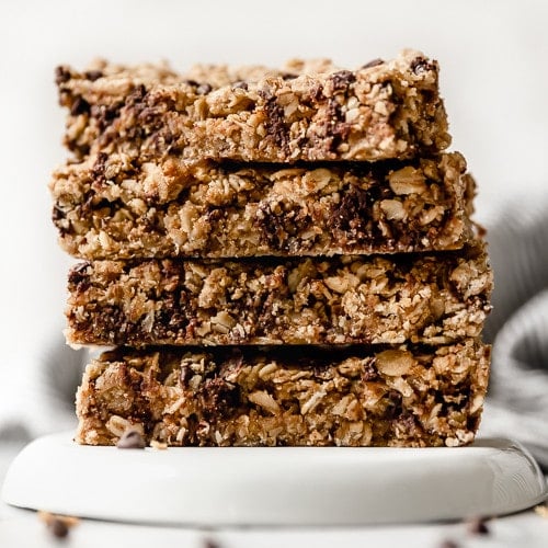 Four peanut butter baked granola bars with chocolate chips stacked on top of each other on a white plate