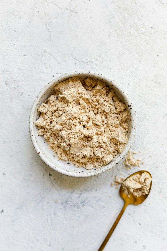 Whey protein powder in a speckled bowl with a spoonful of whey powder on a gold spoon.