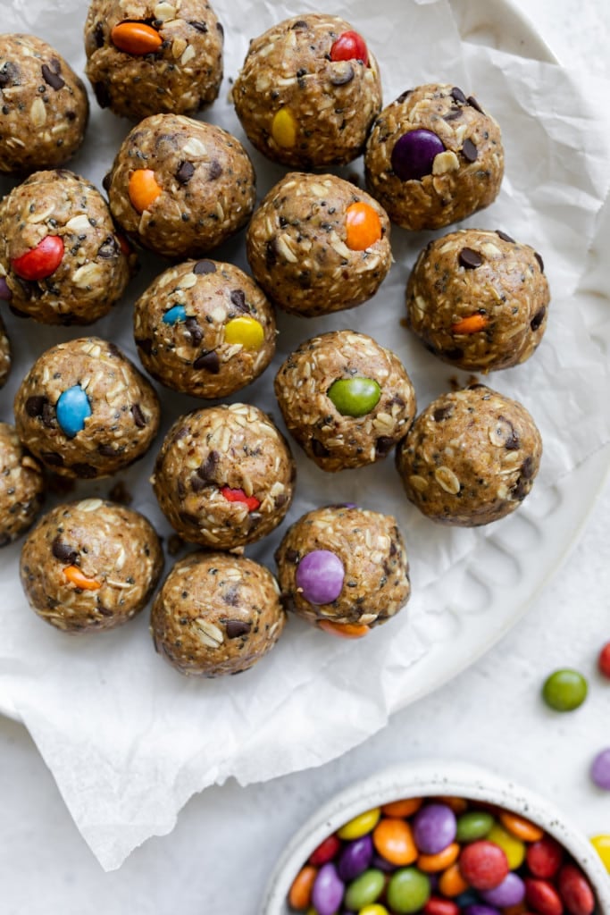 Close up view monster cookie peanut butter protein balls with colorful candy pieces on parchment-covered platter.