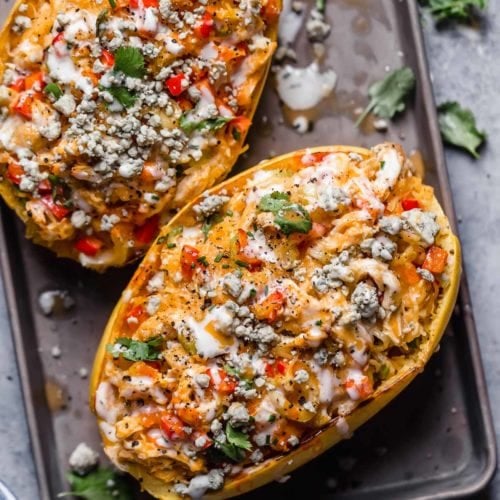 Overhead view spaghetti squash halves filled with buffalo chicken, on baking sheet.