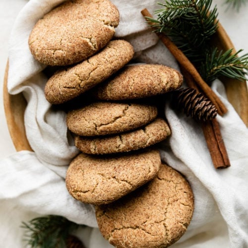 Several snickerdoodle cookies linked up in a box with a white cloth and a sprig of fresh greenery.