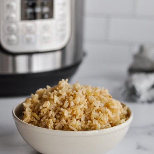A bowl filled with fluffy brown rice on a marble counter with an Instant Pot in the background.