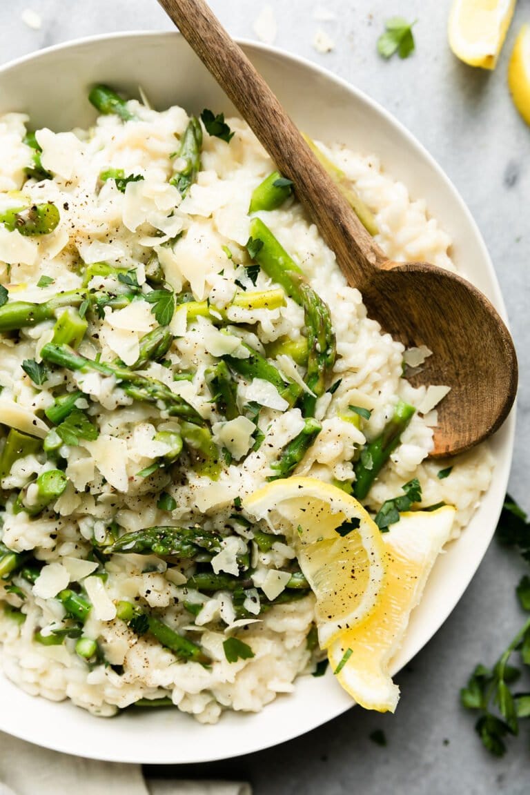 Overhead view creamy lemon asparagus risotto in white serving bowl with wooden spoon