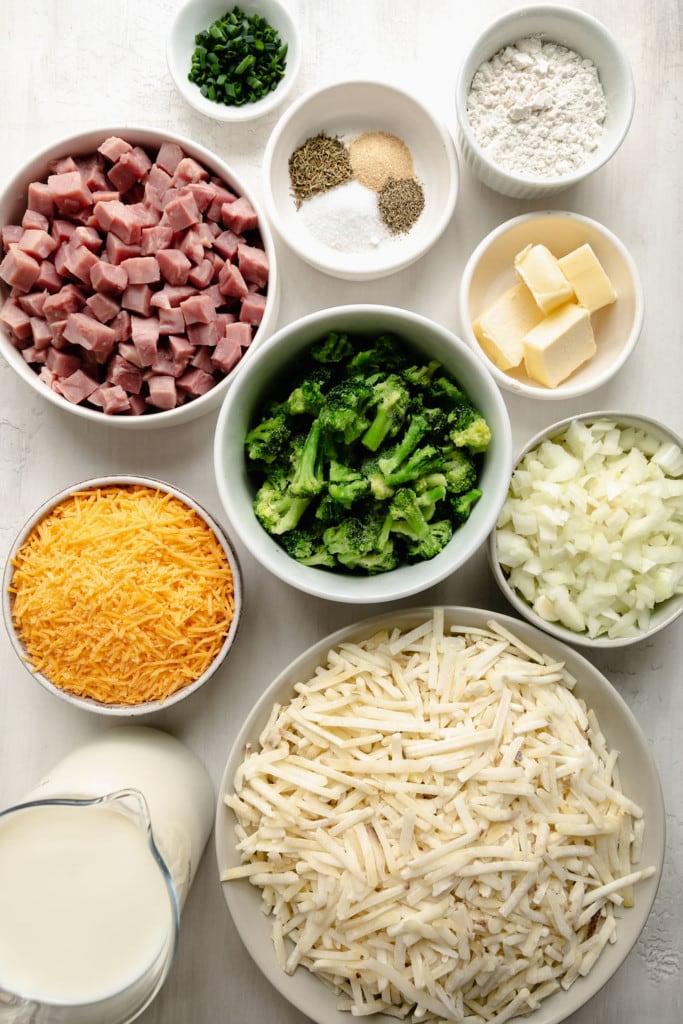 Overhead view of a variety of ingredients in white bowls for cheesy scalloped potatoes. 