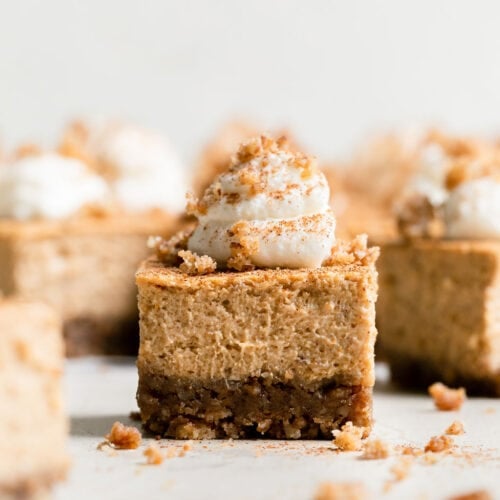 Side view single mini pumpkin cheesecake bar topped with dollop of whipped cream.