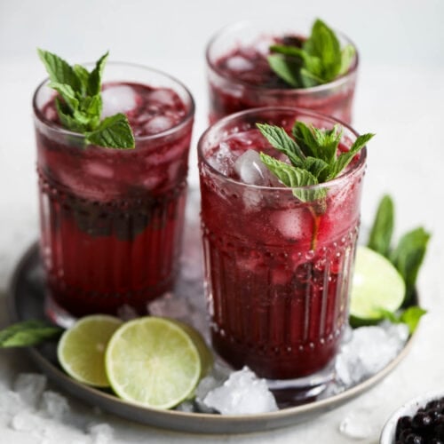Three tall glasses blueberry mojito on silver tray