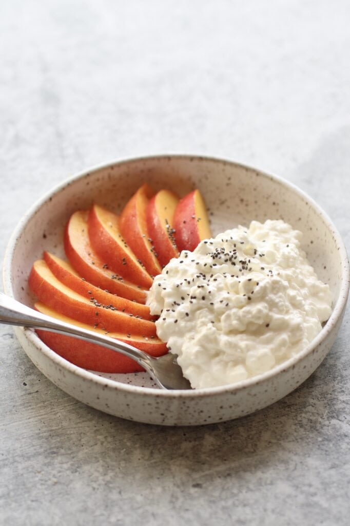 Close up view of a plate of cottage cheese with sliced fruit topped with chia seeds. 