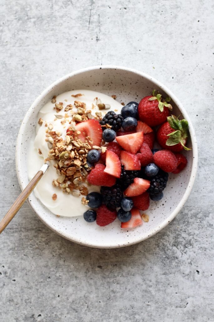 Overhead view of a bowl of yogurt topped with fresh fruit and granola. 